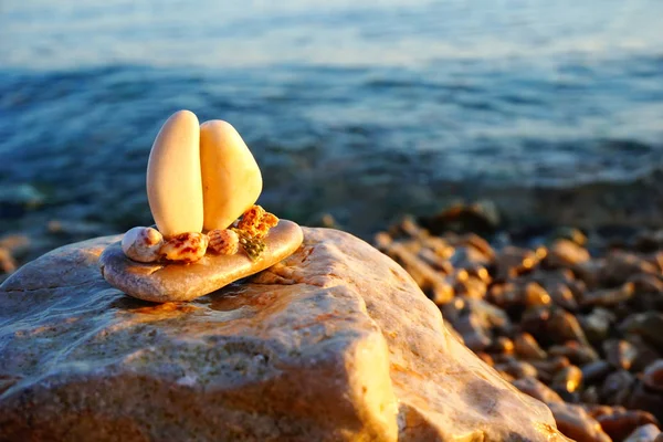 Summer memories background with copy space. Boat made from small stones and decorated with seashells on the rock near the sea beach, lit by sun at sunset