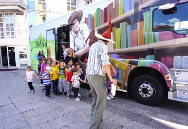Teachers and a group of a preschool children in front of parked open colorful book bus clipart