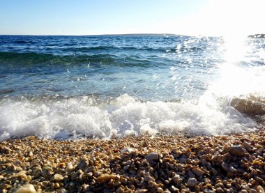 Dalgalı deniz suyu ve beyaz köpük güneş yansıması ile Çakıl plaj