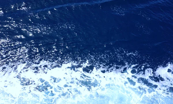 Koyu mavi deniz suyu. Beyaz köpük ve küçük dalgalar ile dalgalı yüzey