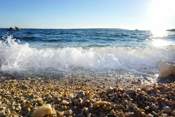 Crystal clear blue sea water with waves and sea foam beating on the shore and pebble beach — Stock Photo, Image