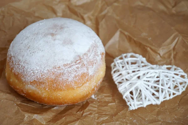 Donut mit weißem gemahlenem Zucker auf dem Backpapier mit weißem Herz verziert — Stockfoto