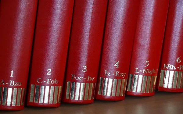 six volumes of red book spines with gold printed letters and numbers on the bookshelf