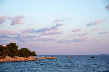 Mandre, Hırvatistan, 25 Temmuz 2020. Dalgalı mavi deniz ve deniz kıyısında güneşlenen insanlar.