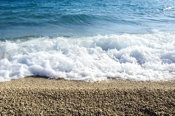 美丽的白色泡沫海浪在蓝色海面和卵石海滩之间摇曳而起 — 图库照片