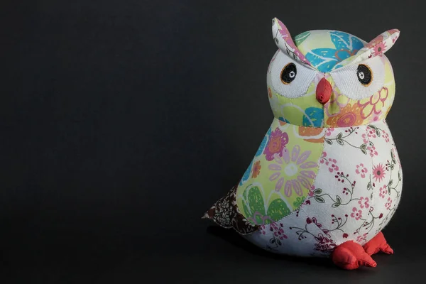 Owl toy on a black background. Wise owl in the night with place for text. Picture for wallpaper and design