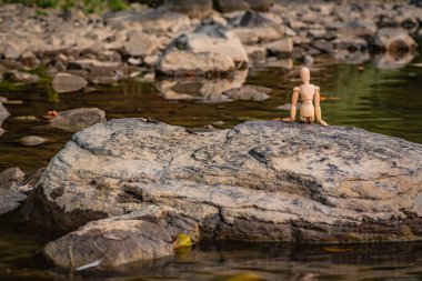 Nehir kıyısında ki bir taşın üzerinde oturan mafsallı küçük adam