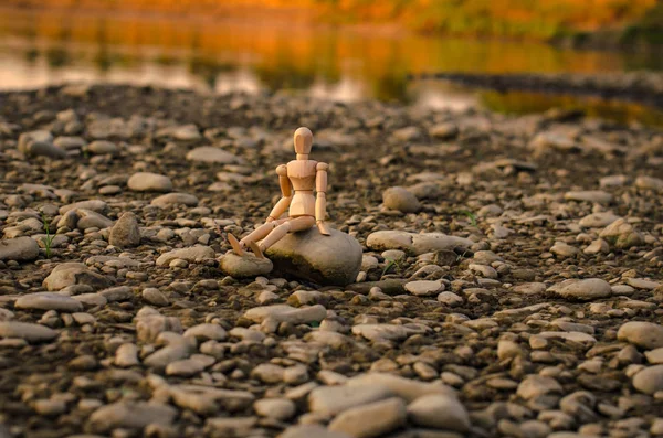 Nehir kıyısında ki bir taşın üzerinde oturan mafsallı küçük adam