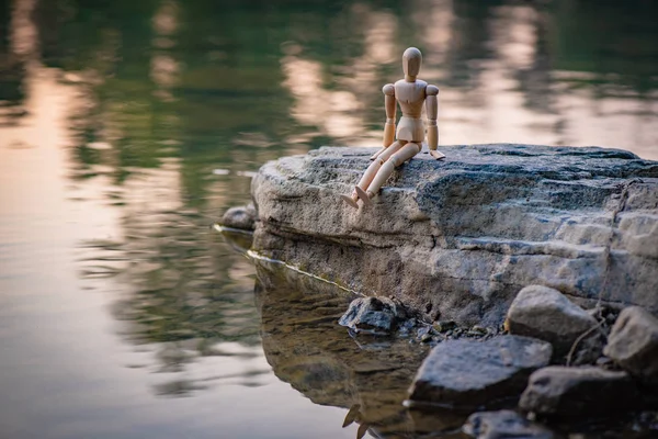 Nehir kıyısında ki bir taşın üzerinde oturan mafsallı küçük adam