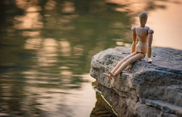 Articulated little man sitting on a stone by the river