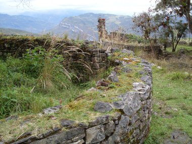 Kuelap kalesinin üçüncü katında dairesel bir evin duvarları, orman ağaçları ve etkileyici And dağları.