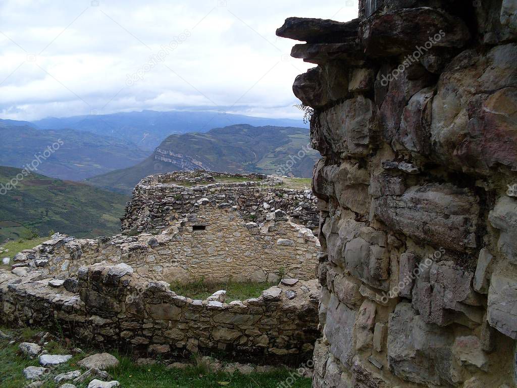 Three circular houses on the third level of Kuelap fortress, cloudy sky, vegetation and breathtaking view of the Andean mountains