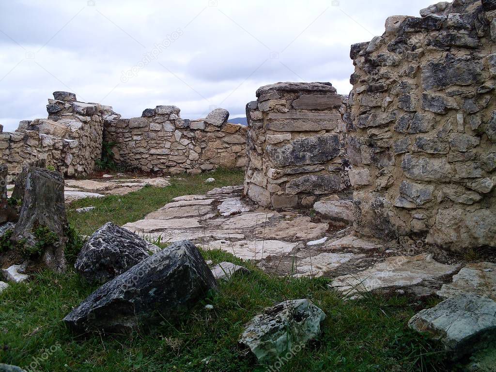 Circular houses on the third level of Kuelap fortress, scattered stones and cloudy sky