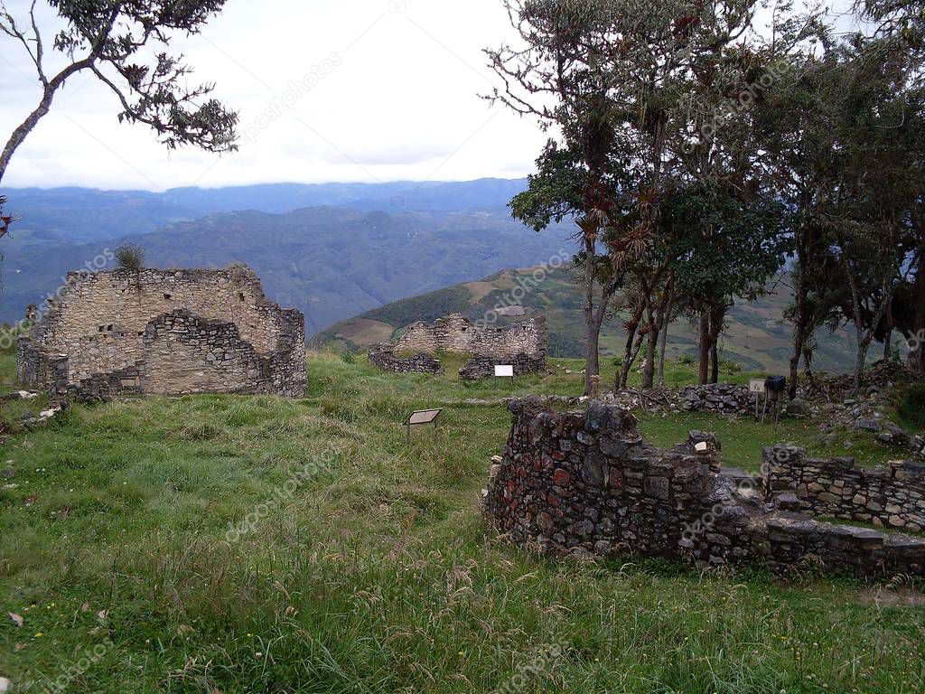 Three circular houses of the Kuelap fortress in the middle of the forest near a precipice, cloudy sky and extraordinary view of the Andes mountain range