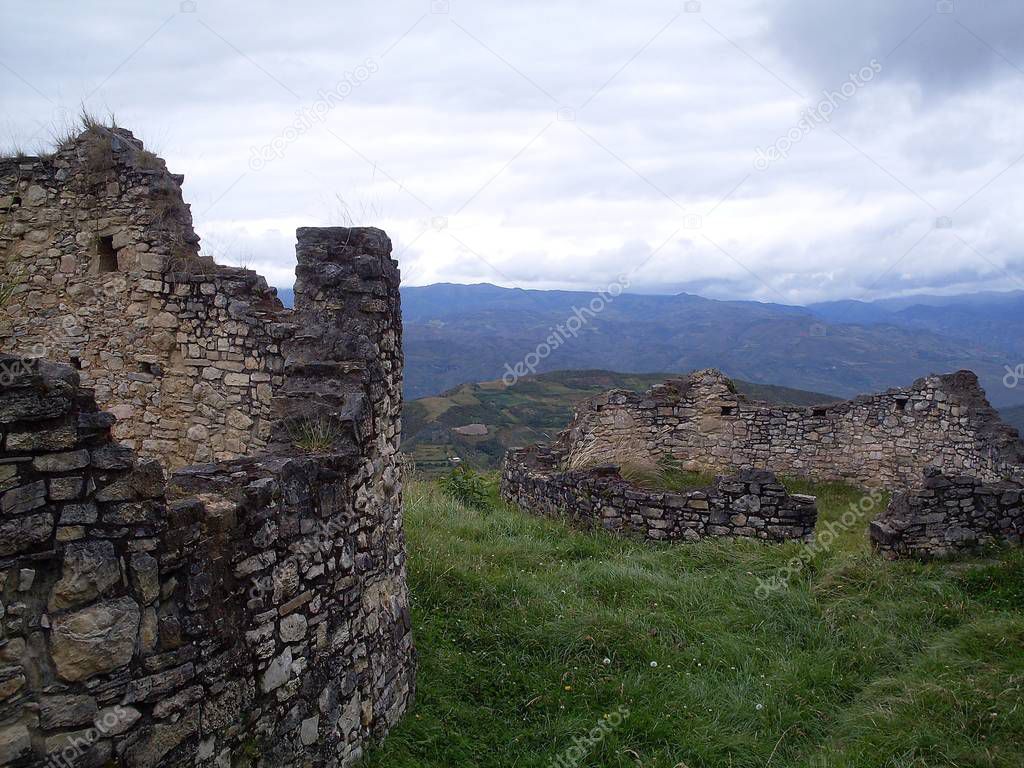 Two circular houses on the third level of the Kuelap fortress, cloudy sky, vegetation and breathtaking view of the Andean mountains