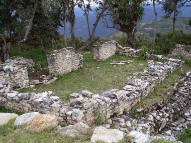 Kuelap Kalesi 'nin dikdörtgen bir evinin kalıntıları. Bulutlu gökyüzü, dağlar ve yemyeşil bitki örtüsü