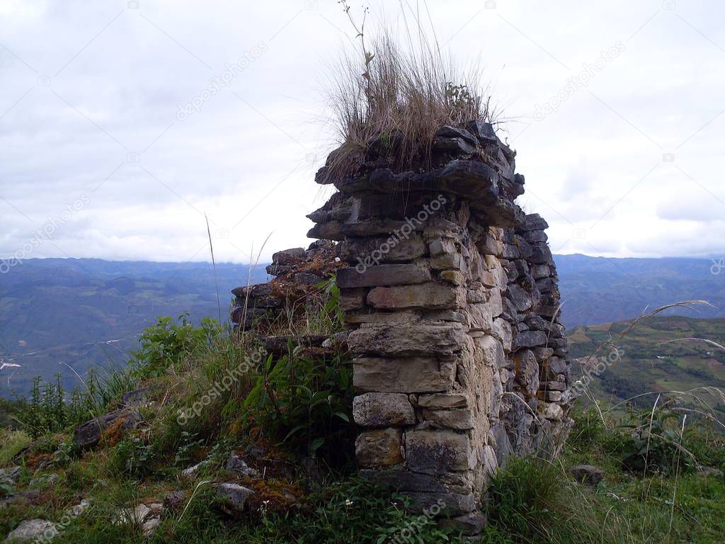 Ruins of a circular house of the fortress of Kuelap. Cloudy sky, mountains and lush vegetation