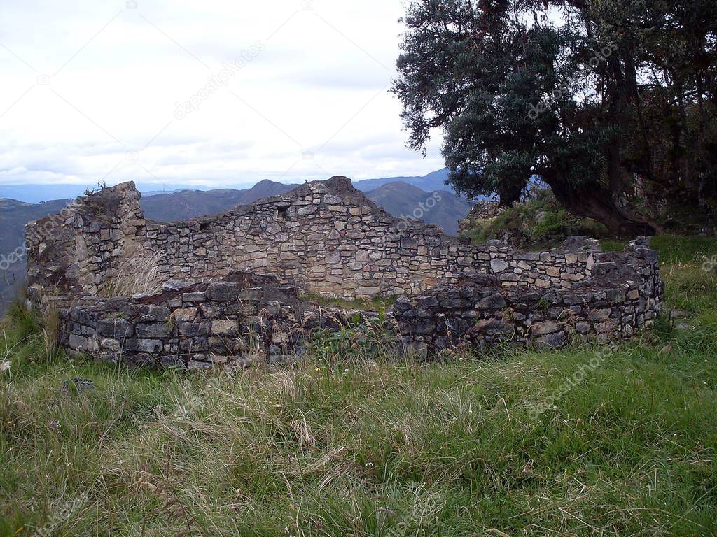 Remains of a circular house on the third level of the Kuelap fortress, forest trees overlooking the Andean mountains in the background on a cloudy day