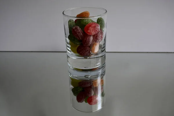 Multicolored tasty candies in a glass cup on the mirror. The reflection of the glass and sweets creates a striking effect of volume and increases the number of objects in the frame, which makes sweets very tasty in appearance.