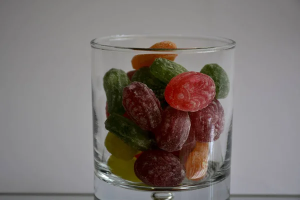 Multicolored tasty candies in a glass cup on the mirror. The reflection of the glass and sweets creates a striking effect of volume and increases the number of objects in the frame, which makes sweets very tasty in appearance.