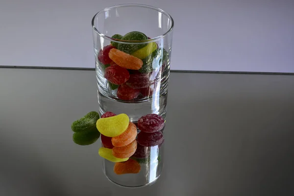 Multicolored tasty candies in a glass cup on the mirror. The reflection of the glass and sweets creates a striking effect of volume and increases the number of objects in the frame, which makes sweets very tasty in appearance.