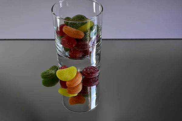 Multicolored tasty candies in a glass cup on the mirror. The reflection of the glass and sweets creates a striking effect of volume and increases the number of objects in the frame, which makes sweets very tasty in appearance.