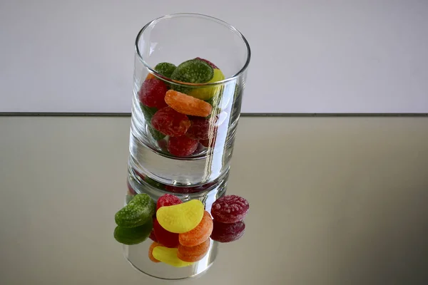 Multicolored tasty candies in a glass cup on the mirror. The reflection of the glass and sweets creates a striking effect of volume and increases the number of objects in the frame, which makes sweets very tasty in appearance.