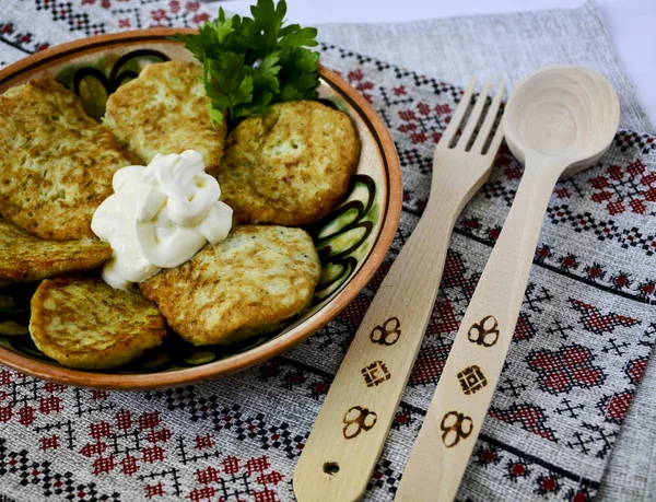 Traditional Slavic cuisine potato pancakes. Potato pancakes. Food served on a clay plate with sour cream. In ancient times, a wooden spoon and a wooden fork were sold. The towel is decorated with a na