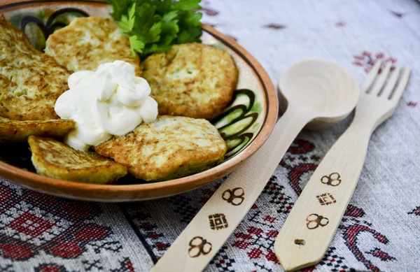 Traditional Slavic cuisine potato pancakes. Potato pancakes. Food served on a clay plate with sour cream. In ancient times, a wooden spoon and a wooden fork were sold. The towel is decorated with a national pattern.