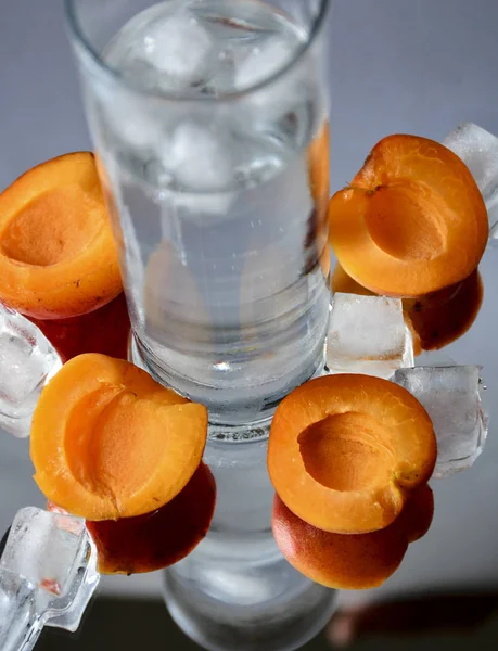 Ice and fruits. Apricots and plums fruits lie on a mirror surface with ice cubes. The water from the melting ice and the fruits reflected in the mirror create a wonderful composition.