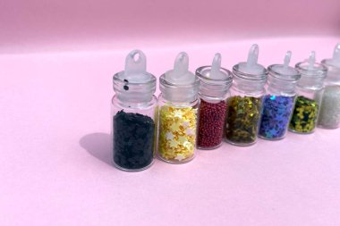 Küçük cam kavanozlarda çivi sanatı ve makyaj için renkli simler. Moda ve güzellik konsepti, pembe arka plan