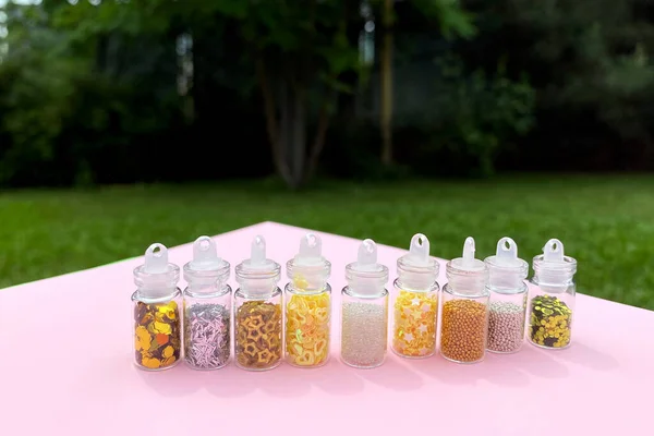 Colorful glitters for nail art and makeup in small glass jars isolated. Fashion and beauty concept, natural and pink background