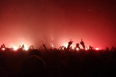 Konserde elleri havada seyirciler ve sahneden ışıklar yükseliyor. Kırmızı ışıklar.