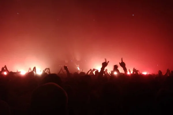 Audience with hands raised at a concert and lights streaming from the stage. Red lights.