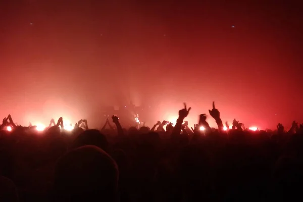 Konserde elleri havada seyirciler ve sahneden ışıklar yükseliyor. Kırmızı ışıklar.
