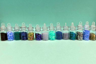 Küçük cam kavanozlarda çivi sanatı ve makyaj için renkli simler. Moda ve güzellik konsepti, açık yeşil arka plan