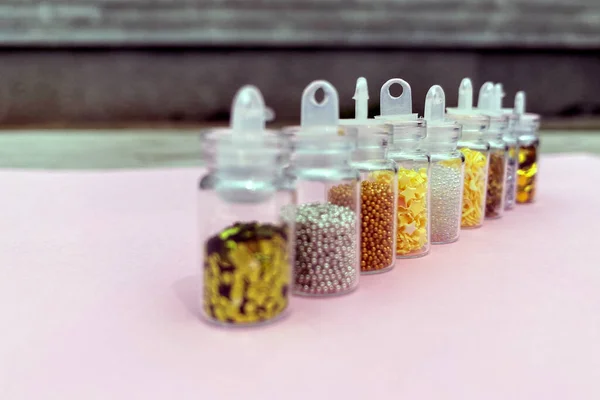 Colorful glitters for nail art and makeup in small glass jars isolated. Fashion and beauty concept, natural and pink background
