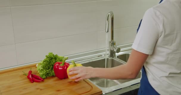 Back view. Close-up shooting. Womens hands are washing yellow pepper and broccoli in the washbasin. 4k — Stock Video