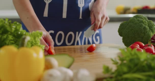 Tiroteio de perto. Uma mulher está cortando tomates cereja em uma placa de cozinha. Há muitos vegetais por aí. 4K — Vídeo de Stock