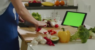 Kadın vişneli domates dilimliyor ve tablete bakıyor. Yeşil ekranlı tablet. Salata hazırlığı. 4K
