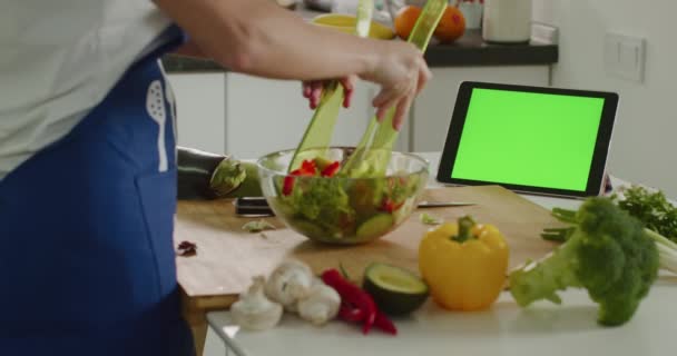 Die Frau mixt den Salat und schaut auf die Tablette. Tablet mit grünem Bildschirm. Salatzubereitung. 4K — Stockvideo