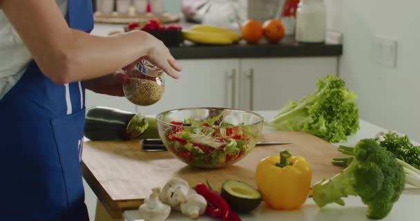 Prise de vue rapprochée. Une femme saupoudre des graines de sésame sur la salade. Préparation des salades. 4K — Video