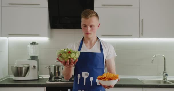 Un homme réfléchit à ce qu'il faut choisir. Salade ou chips. Nourriture saine ou malbouffe. 4K — Video