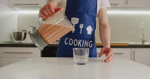 Penembakan jarak dekat. Seorang pria menuangkan smoothie siap pakai dari mangkuk blender ke dalam gelas. Membuat smoothie. 4K — Stok Video