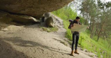 Adam büyük kayanın altında duruyor ve rotayı kontrol ediyor. Yürüyüş. 4k