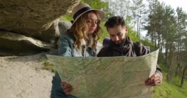 Bir adam ve bir kız bir kayanın altında duruyorlar ve haritada ilginç yerler arıyorlar. Yürüyüş. 4k