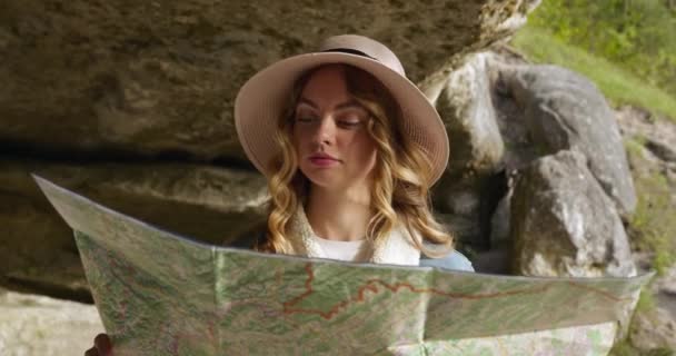 Prise de vue rapprochée. La jeune fille se tient sous une grande pierre et cherche des endroits intéressants sur la carte. Randonnée. 4K — Video