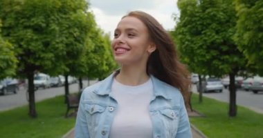 Yakın plan çekim. Gülümseyen bir kız sokakta yürüyor ve kameraya bakıyor. Saçları rüzgarda uçuşuyor. 4K