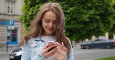 Yakın plan çekim. Kız ayakta duruyor ve mesaj atıyor. Ona yazdıklarıyla gülüyor. 4K