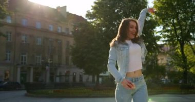 Neşeli bir kız dansa gidiyor. O gülüyor ve büyük kulaklıklarla müzik dinliyor. Saçları rüzgarda dalgalanıyor. Yaz güneşi parlıyor. 4K